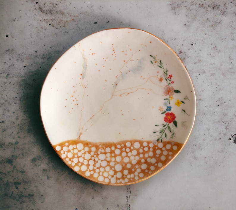 May include: A white ceramic plate with a gold rim and a floral design. The plate has a brown and white speckled pattern around the edge.