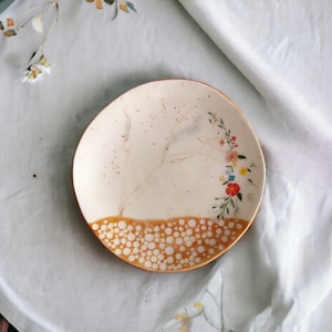 May include: A white ceramic plate with a brown rim and a floral design. The plate has a speckled brown glaze and a pattern of white dots on the rim.
