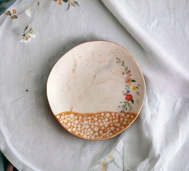 May include: A white ceramic plate with a brown rim and a floral design. The plate has a speckled brown glaze and a pattern of white dots on the rim.