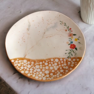 May include: A white ceramic plate with a brown and white speckled design and a floral pattern in shades of pink, orange, yellow, and blue.
