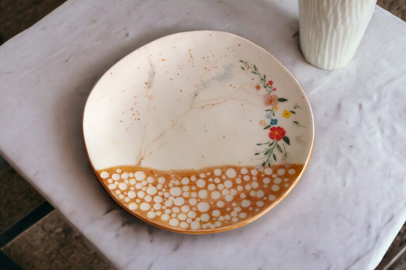 May include: A white ceramic plate with a brown and white speckled design and a floral pattern in shades of pink, orange, yellow, and blue.