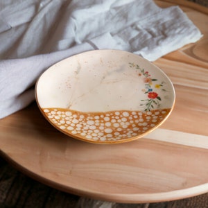 May include: A white ceramic plate with a brown and white speckled design and a floral pattern around the rim. The plate is on a wooden surface.