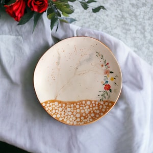 May include: A white ceramic plate with a brown rim and a floral design. The plate has a speckled brown glaze and a pattern of white dots around the rim.