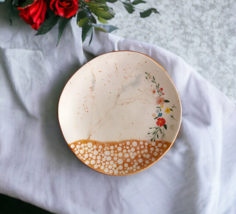 May include: A white ceramic plate with a brown rim and a floral design. The plate has a speckled brown glaze and a pattern of white dots around the rim.