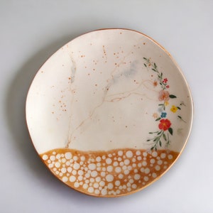 May include: A white ceramic plate with a brown rim and a floral design. The plate has a speckled brown glaze and a pattern of white dots on the bottom edge.