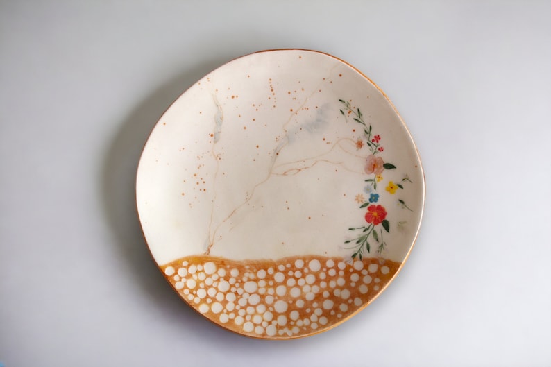 May include: A white ceramic plate with a brown rim and a floral design. The plate has a speckled brown glaze and a pattern of white dots on the bottom edge.