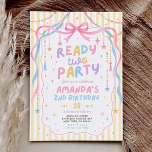 May include: A rectangular birthday invitation card featuring a yellow and white striped background with a pink bow, blue and pink ribbons, and hanging star and bead decorations. The text reads READY two PARTY, AMANDA'S 2nd BIRTHDAY, and event details.