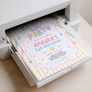 May include: A white printer outputting a birthday invitation with yellow stripes, pink and blue text reading READY TWO PARTY AMANDA'S 2ND BIRTHDAY, and colourful star and tassel graphics. The invitation includes event details like date, time, and location.