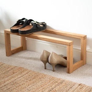 May include: A wooden shoe rack with two tiers. The top tier has a pair of black sandals and the bottom tier has a pair of beige heels.
