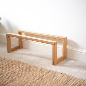 May include: Two wooden shelves made of light brown wood. The shelves are stacked on top of each other and are supported by four legs. The shelves are sitting on a light brown rug.