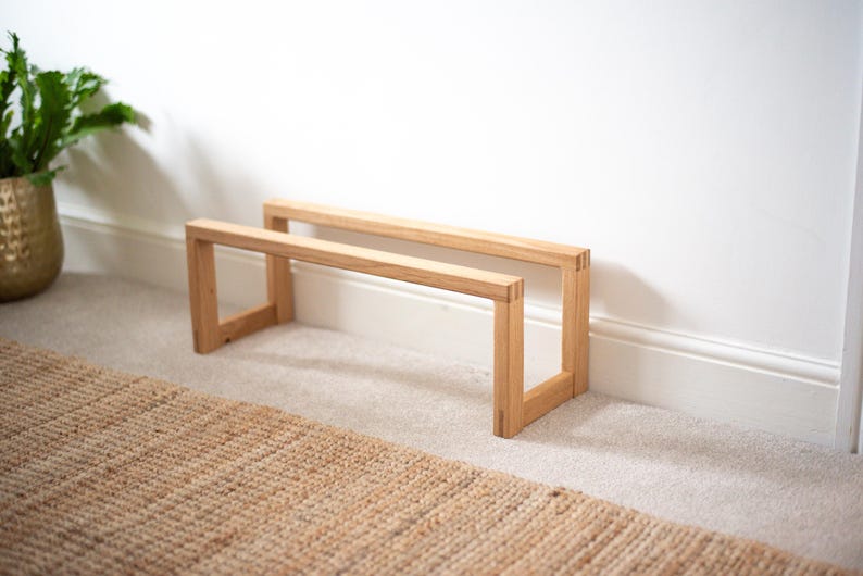 May include: Two wooden shelves made of light brown wood. The shelves are stacked on top of each other and are supported by four legs. The shelves are sitting on a light brown rug.