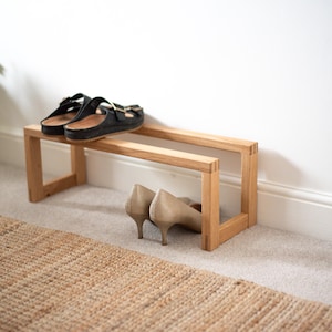 May include: A wooden shoe rack with two tiers. The top tier has a pair of black sandals on it, and the bottom tier has a pair of beige heels.