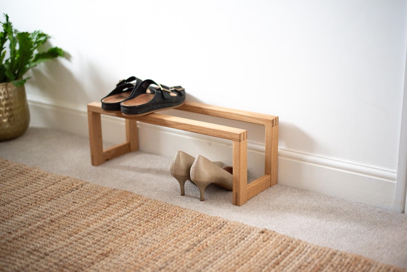 May include: A wooden shoe rack with two tiers. The top tier has a pair of black sandals on it, and the bottom tier has a pair of beige heels.