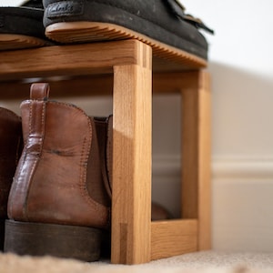 May include: A wooden shoe rack with two shelves. The top shelf has a pair of black shoes and a pair of brown shoes. The bottom shelf has a pair of brown boots and a pair of brown shoes.