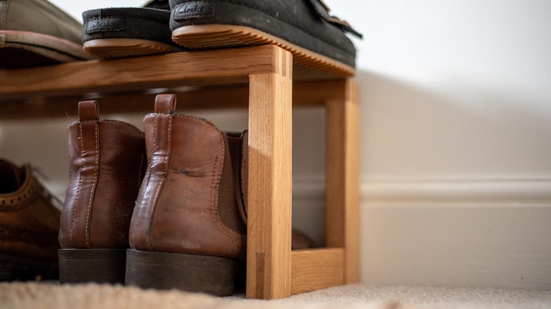 May include: A wooden shoe rack with two shelves. The top shelf has a pair of black shoes and a pair of brown shoes. The bottom shelf has a pair of brown boots and a pair of brown shoes.
