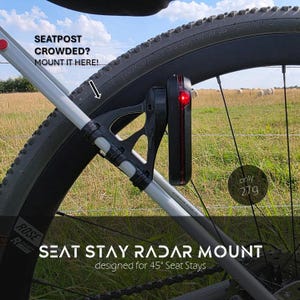 Könnte beinhalten: Eine schwarze Kunststoffhalterung für Fahrrad-Radar am Sitzstreben. Die Halterung trägt ein rotes Licht und zeigt den Text SEATPOST CROWDED? MOUNT IT HERE! sowie SEAT STAY RADAR MOUNT designed for 45° Seat Stays, mit einem Gewicht von nur 27g.