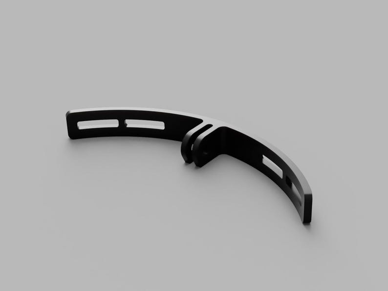 May include: A black, curved mounting bracket featuring a central hinge connector with two parallel tabs and elongated rectangular slots along each arm. The component has a smooth, matte finish and a semi-circular design for attachment purposes.