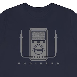 Puede incluir: Camiseta azul marino con un gráfico gris de un multímetro y la palabra "ENGINEER" debajo. El gráfico del multímetro tiene el texto "ELECTRICAL ELECTRICAL ELECTRICAL ELECTRICAL ELECTRICAL" en su interior. El diseño es simple y limpio.