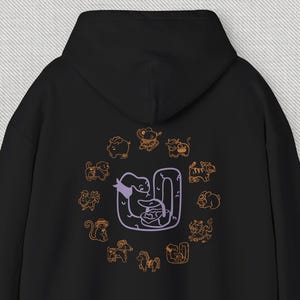 Op de afbeelding: Zwarte hoodie met een paars en oranje ontwerp van de Chinese dierenriemdieren op de rug. De slang bevindt zich in het midden van het ontwerp.