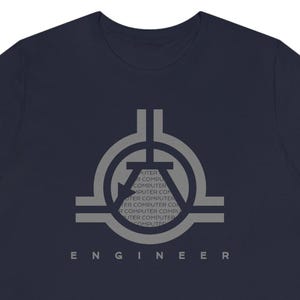 Könnte beinhalten: Marineblaues T-Shirt mit grauem Grafikdesign. Das Design zeigt ein stilisiertes Symbol und das Wort "ENGINEER" in einer serifenlosen Schriftart. Das Wort "COMPUTER" wird wiederholt.