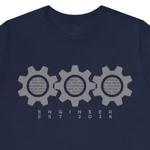 May include: Navy blue t-shirt featuring three gray gear graphics. The gears have the words "MECHANICAL" and "ENGINEER" printed inside. Below the gears, the text "ENGINEER EST. 2026" is printed in gray.