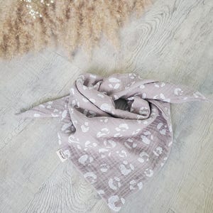 Könnte beinhalten: Ein mauvefarbenes Bandana-Tuch mit weißem Leopardenmuster. Das Tuch besteht aus einem weichen, leichten Stoff und ist dreieckig gefaltet. Das Tuch liegt auf einer hellen Holzoberfläche.