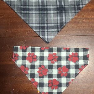 May include: Two dog bandanas. The top bandana is gray and black plaid. The bottom bandana is white and black checkered with red paw prints.