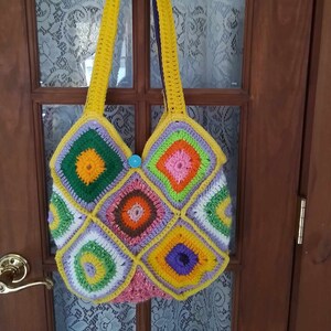 May include: A crocheted tote bag with a yellow strap and a colorful patchwork design. The bag is made of squares in shades of green, pink, orange, purple, and white.