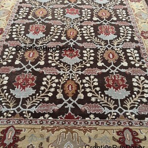 May include: A brown area rug with a floral pattern in shades of red, beige, and white. The rug has a border with a more intricate design. The text "CreativeRugDecor" appears three times on the rug.