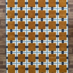 May include: A rectangular rug with a geometric pattern. The design features squares in shades of brown, navy blue, and light blue. The rug is made of a soft material and is suitable for a living room or bedroom.