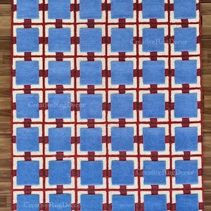 May include: A rectangular rug with a repeating geometric pattern. The design features light blue squares, red cross-like shapes, and white borders. The words "Creative Rug Decor" are printed on the rug.