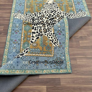 May include: A rectangular rug with a light blue border and a central design featuring a leopard pattern. The leopard design is in black and white spots. The rug has the text "CreativeRugDecor" in multiple places.