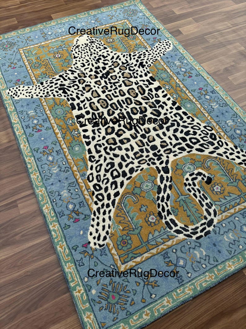 May include: A rectangular rug with a light blue border and a central design resembling a leopard skin. The leopard pattern is black and brown spots on a cream background. The rug has a decorative border with floral patterns.