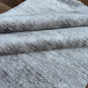 May include: A gray and white rug with a soft, textured surface. The rug has a subtle sheen and a fringed edge.