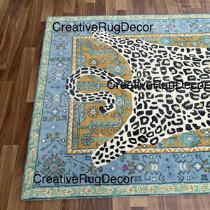 May include: A rectangular rug with a leopard design. The rug features a light blue border with floral patterns, a mustard yellow center, and a white leopard with black spots. The text "Creative Rug Decor" is visible.