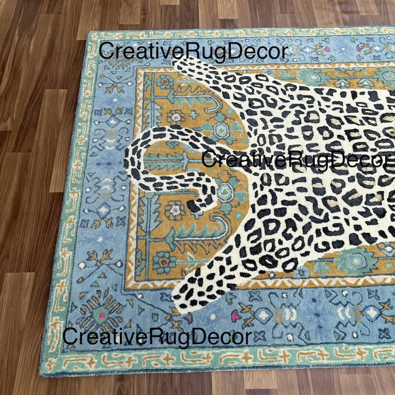 May include: A rectangular rug with a leopard design. The rug features a light blue border with floral patterns, a mustard yellow center, and a white leopard with black spots. The text "Creative Rug Decor" is visible.