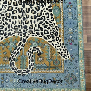 May include: A rectangular rug with a leopard print design in cream and black. The rug has a blue border with floral and geometric patterns, and the text "Creative Rug Decor".