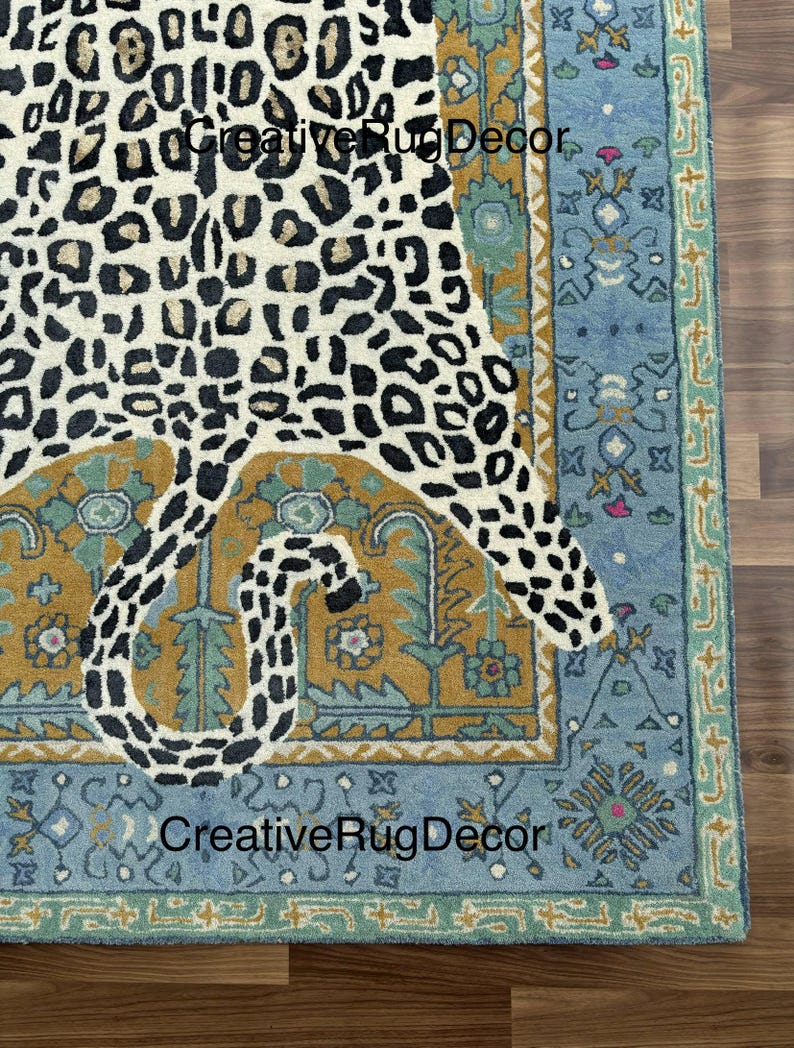 May include: A rectangular rug with a leopard print design in cream and black. The rug has a blue border with floral and geometric patterns, and the text "Creative Rug Decor".