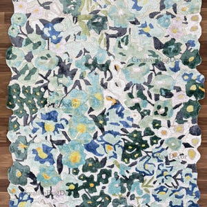 May include: A floral area rug with a white background and a pattern of blue, green, and yellow flowers. The rug has a unique, irregular edge and is designed to add a touch of nature to any room.