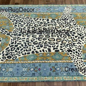 May include: A rectangular rug with a leopard print design in the center. The leopard print is black and white. The rug has a blue and gold border with floral patterns. The text "CreativeRugDecor" is visible on the rug.