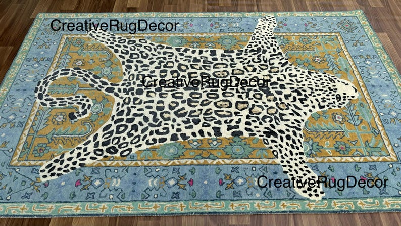 May include: A rectangular rug with a leopard print design in the center. The leopard print is black and white. The rug has a blue and gold border with floral patterns. The text "CreativeRugDecor" is visible on the rug.