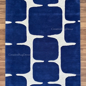 May include: A rectangular rug with a bold, geometric design. The rug features a deep blue background with a repeating pattern of white, rounded shapes. The rug is placed on a wooden floor.