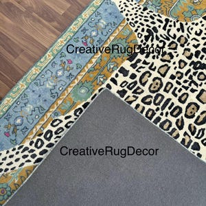 May include: Overhead view of a rug with a leopard print pattern in black and tan, and a blue and gold patterned border. The rug is partially rolled up, revealing a gray backing. The text "CreativeRugDecor" is visible.