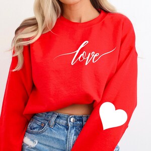 May include: Red cropped sweatshirt with the word "love" in white script on the front and a white heart on the left sleeve.