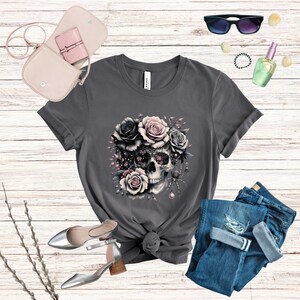 May include: A charcoal grey t-shirt with a graphic of a skull with pink and black roses. The skull is surrounded by vines and a spider.