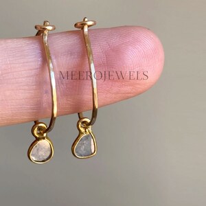 Op de afbeelding: Gouden creolen met een klein, traanvormig diamanten hanger. De oorbellen zijn simpel en elegant.