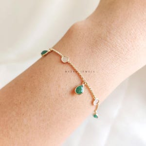 May include: A gold chain bracelet with alternating green and white teardrop-shaped stones. The bracelet is on a person's wrist. "MEERU JEWELS" is printed on the wrist.