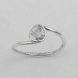 May include: A silver ring featuring a clear, faceted gemstone set in a simple, curved band. The ring is a delicate and minimalist design.
