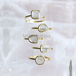以下が含まれることがあります： 透明なファセットカットの宝石がセットされたゴールドリングが4つ。リングは重ねて置かれており、一番上が一番大きく、一番下が一番小さい。すべてのリングはシンプルなゴールドバンドにセットされています。