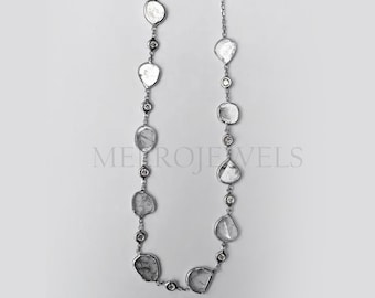 Puede incluir: Un collar de plata con piedras preciosas claras de forma irregular y pequeñas piedras preciosas claras redondas. El collar se muestra sobre un fondo blanco. Es una delicada pieza de joyería.